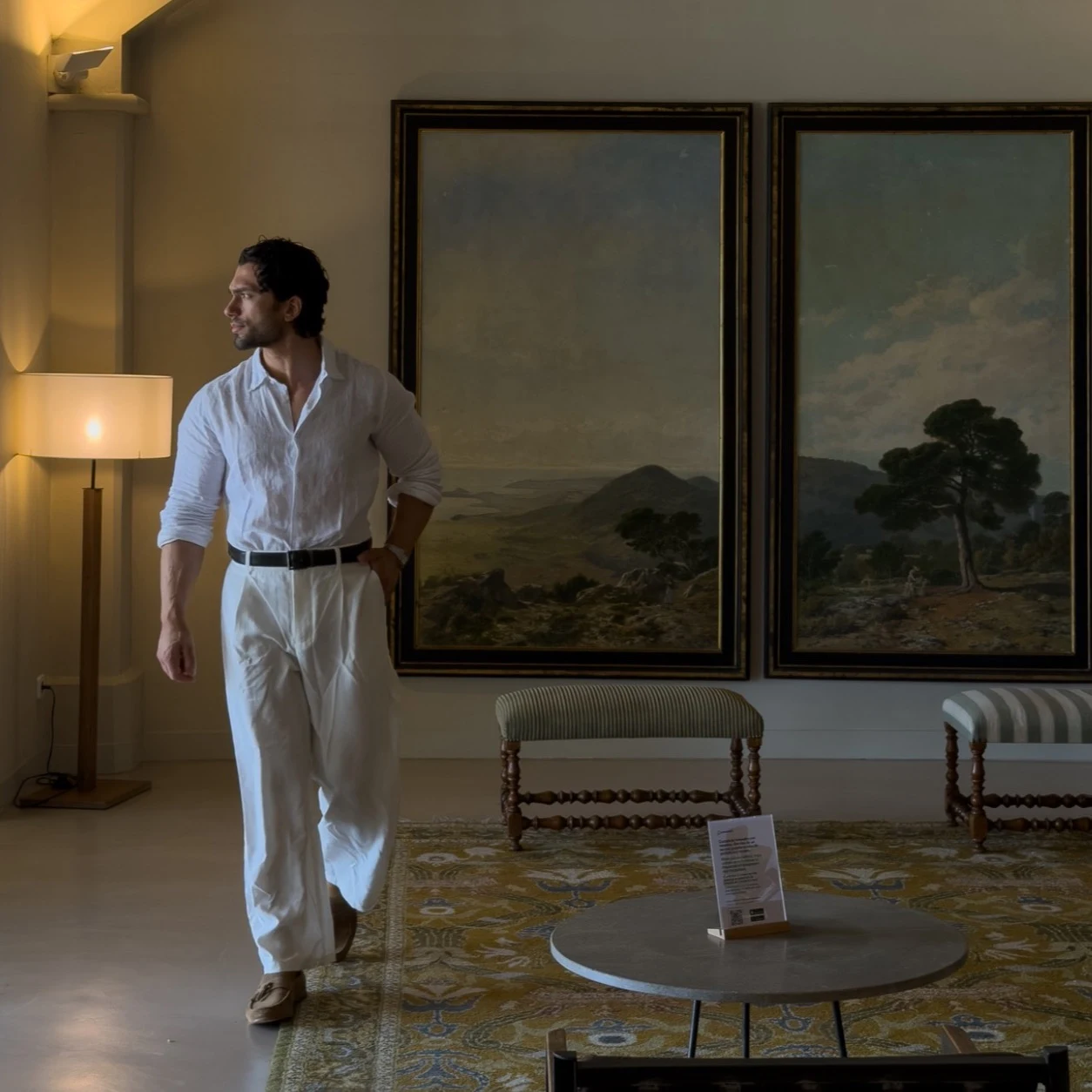 Marino in a white shirt and trousers, standing in a warmly lit room